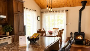 Una cocina con armarios de madera, encimera de granito, una isla central con sillas, una mesa de comedor y un estufa de leña.