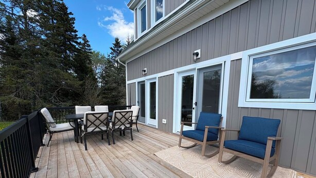 A deck with outdoor furniture, a railing, and a building with large windows and a door. - Otter Cove Cottage, completely renovated house on Campobello (Wilsons Beach)