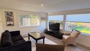 A living room with a sofa, a coffee table, a TV, and a wicker chair. - Otter Cove Cottage, completely renovated house on Campobello (Wilsons Beach)