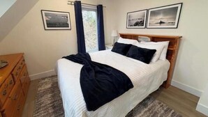 A bedroom with a bed, a dresser, a window with curtains, and two framed pictures on the wall. - Otter Cove Cottage, completely renovated house on Campobello (Wilsons Beach)