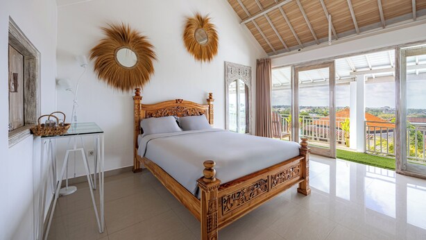 Ein Schlafzimmer mit einem großen Bett, einem Glastisch, einem Spiegel und Blick ins Freie.