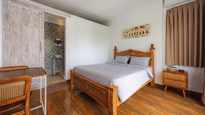 Ein Schlafzimmer mit einem hölzernen Bett, einem Esstisch, einem Stuhl, einem kleinen Beistelltisch und einem Badezimmer mit einer gefliesten Wand.