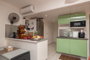 A compact kitchen with a refrigerator, microwave, and a small island with a fan and various kitchen items. - Au Paradis de Sian - Studio Avec Climatisation (Saint-Francois)