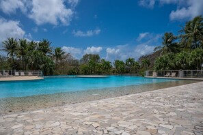 A clear blue pool surrounded by palm trees and a stone deck. - Au Paradis de Sian - Studio Avec Climatisation (Saint-Francois)
