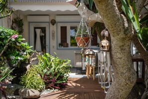A garden with potted plants, a wooden deck, and a building with a door and windows in the background. - Au Paradis de Sian - Studio Avec Climatisation (Saint-Francois)