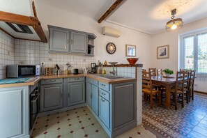 A kitchen with grey cabinets, a microwave, a sink, and a dining area with wooden chairs and a table. - Le Saint Laurent - Avec Piscine Privée (Saint-Laurent-la-Vernède)
