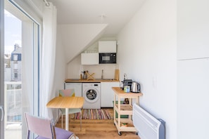 Cocina compacta con lavadora, microondas y un pequeño comedor con mesa y sillas.