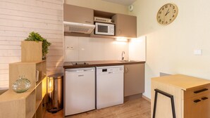 A compact kitchen with built-in appliances, a clock, and a trash bin. - La Bulle d’Ax - Domaine de la Vallée d'Ax (Ax-les-Thermes)