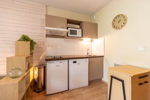 A compact kitchen with built-in appliances, a clock, and a trash bin. - La Bulle d’Ax - Domaine de la Vallée d'Ax (Ax-les-Thermes)