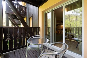 A balcony with a table and chairs, a wooden staircase, and a glass door leading to an outdoor area. - La Bulle d’Ax - Domaine de la Vallée d'Ax (Ax-les-Thermes)