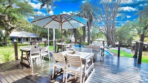 Un patio al aire libre con mesas y sillas, una piscina y palmeras.