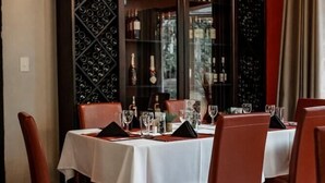 Un comedor con una mesa dispuesta para cuatro personas, rodeada de sillas y una estantería para vinos al fondo.