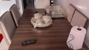 Una mesa de comedor con sillas, un control remoto, una bandeja decorativa y un televisor montado en la pared.