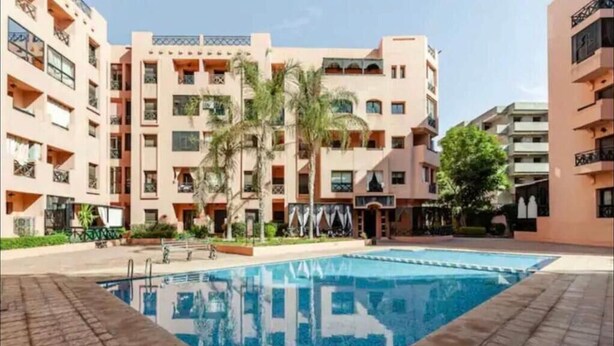 Un hotel de varios pisos con balcones, piscina y palmeras.