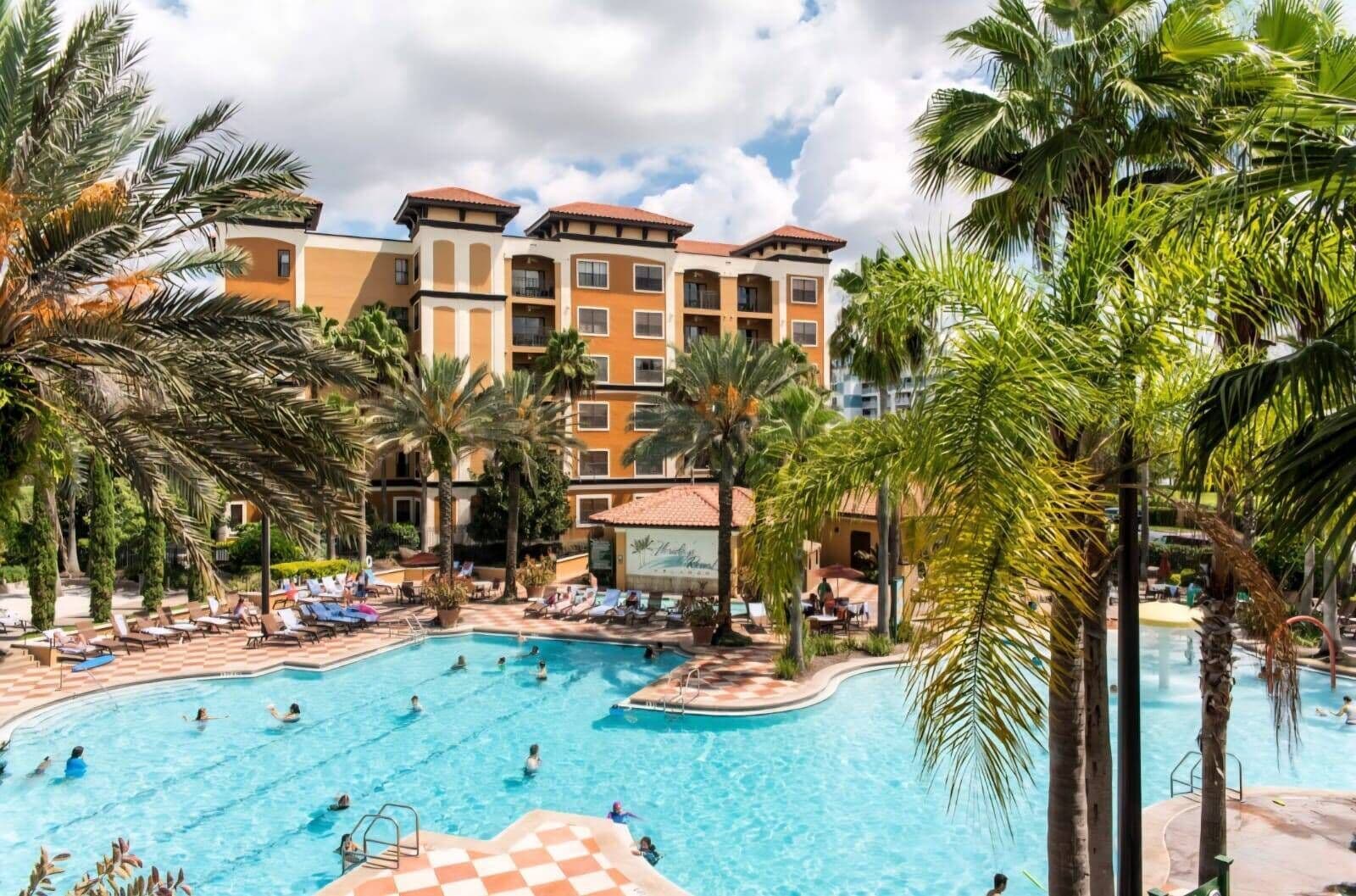 A hotel with a swimming pool surrounded by palm trees and lounge chairs.