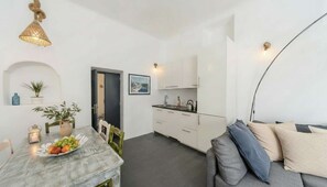 A compact living space with a dining area, kitchenette, and a sofa. - Grand Village Stay for Seven (Santorini)