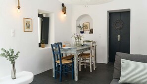A dining area with a wooden table, blue chairs, and a dark door. - Grand Village Stay for Seven (Santorini)