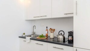 A modern kitchen with white cabinets, a stainless steel sink, a kettle, and a bottle of wine on the counter. - Grand Village Stay for Seven (Santorini)