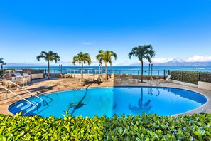 A pool with a clear view of the ocean, surrounded by palm trees and lounge chairs. - Oceanfront Ground-Level Luxe Getaway West Maui (Lahaina)