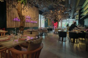 Ein Restaurantinneres mit gedeckten Tischen, einem Bartender, der Getränke zubereitet, und einem leuchtenden Neonzeichen an der Wand.
