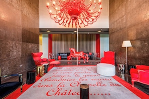 Eine Lobby mit rotem und weißem Teppich, einem Chandelier, roten Sesseln, einem weißen Sofa und einer Statue eines roten Pferdes.