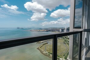 Weitläufige Aussicht aus einem Hochhausfenster auf eine Küstenstadt bei klarem Himmel und einer entfernten Insel.