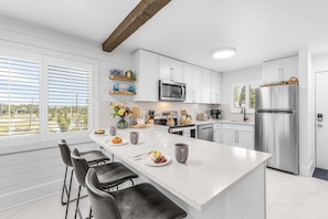 A modern kitchen with white cabinetry, a stainless steel refrigerator, and a large island with bar stools. - Beachfront Escape with Pool, Tiki Huts & Stunning Gulf Views - Casa Bleu - Roelens (Fort Myers Beach)