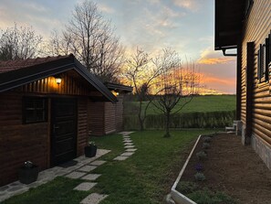 A wooden cabin with a stone pathway leading to a door, surrounded by a grassy yard and trees. - Relax by the Mrežnica River with jacuzzi, sauna and forest view (Mihalić Selo)
