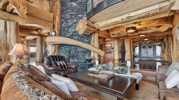A log cabin interior with a stone fireplace, leather furniture, and a large wooden ceiling.