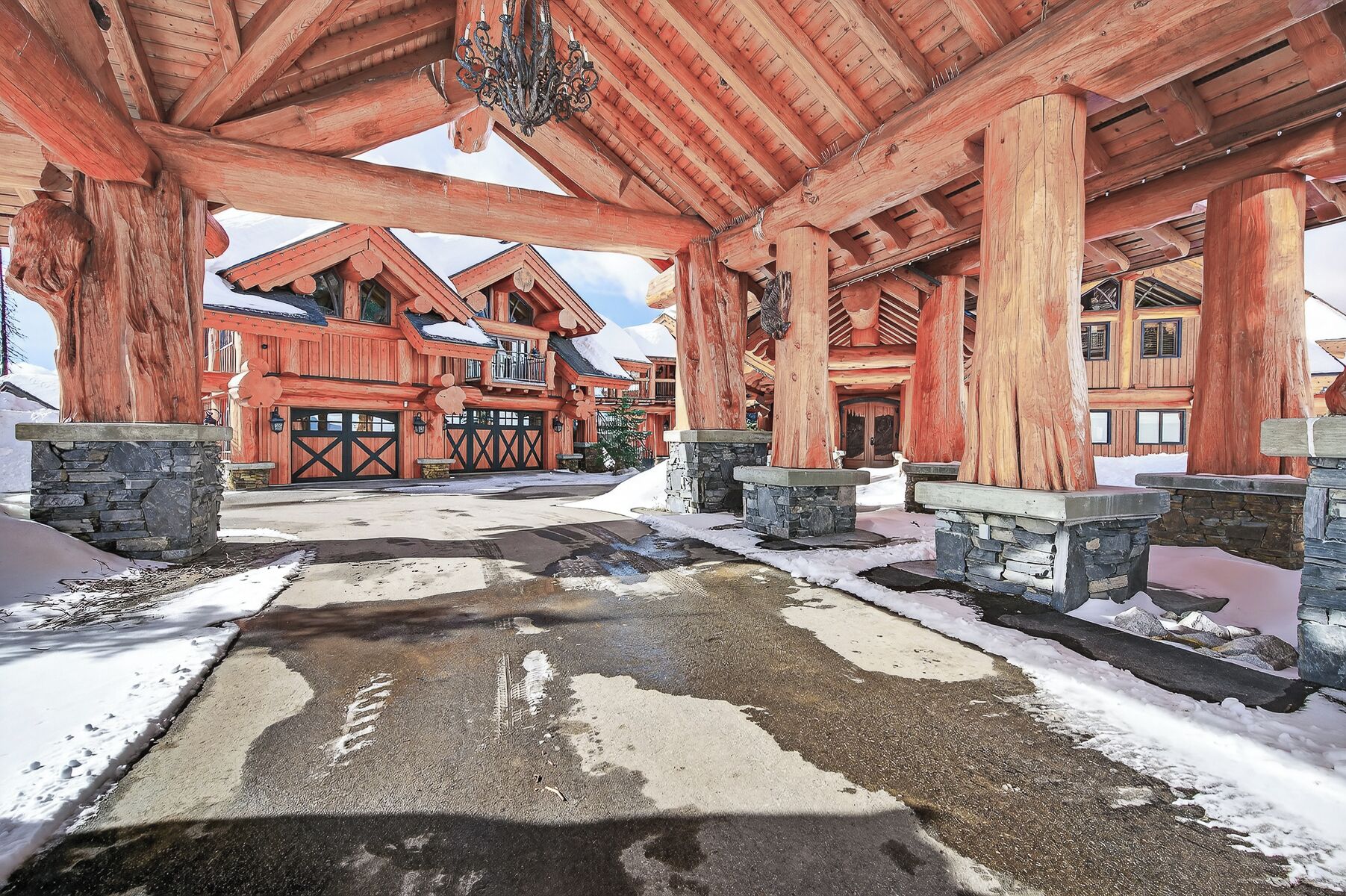 A wooden lodge with a covered entrance, stone pillars, and a snow-covered ground.
