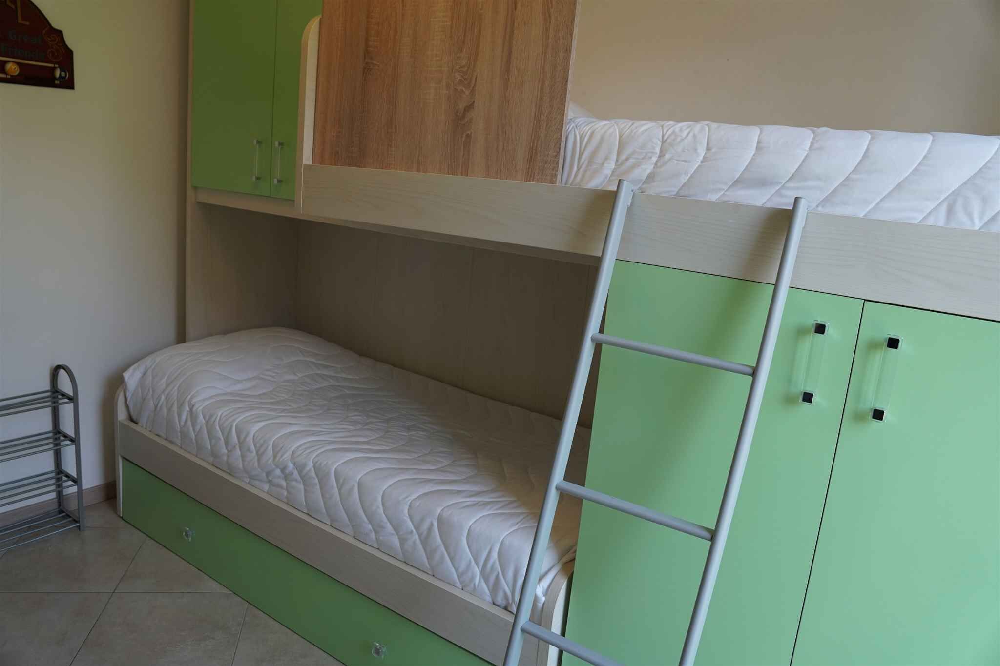 A bunk bed with a ladder, a green wardrobe, and a metal rack.