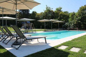 A swimming pool with lounge chairs and umbrellas, surrounded by a grassy area and trees. - Holiday apartment by the water with shared boat dock (Mattarana)