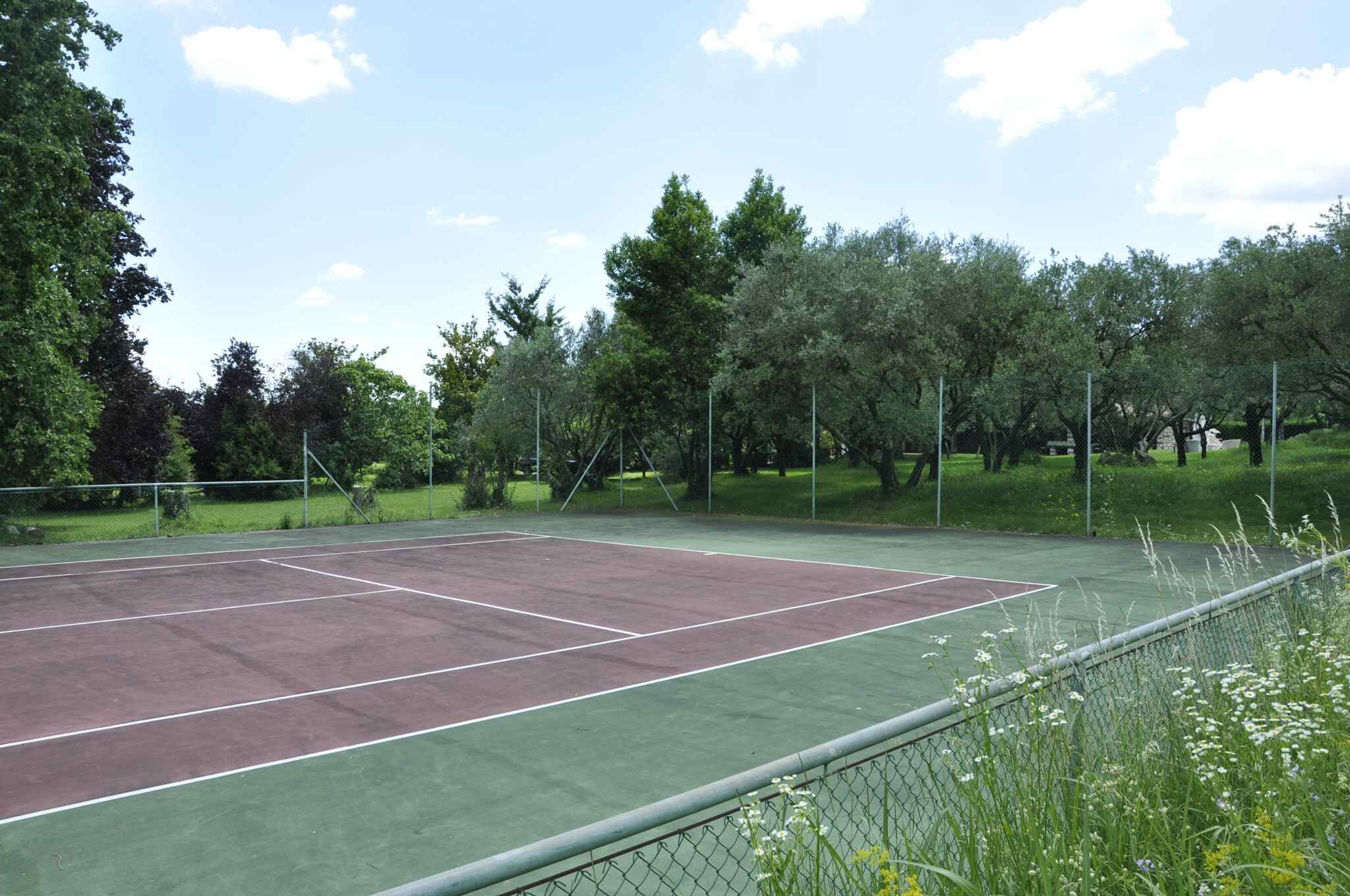Una cancha de tenis al aire libre rodeada de árboles y una valla de malla metálica.