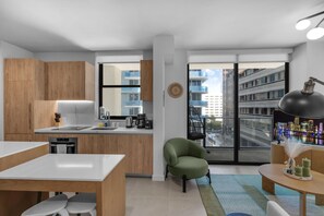 Eine moderne Küche mit Holzschränken, eine Essecke mit weißem Tisch und Blick auf eine Stadtkulisse durch große Fenster.