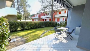 En terrasse med flisegulv, et bord med stole og en hæk i baggrunden.
