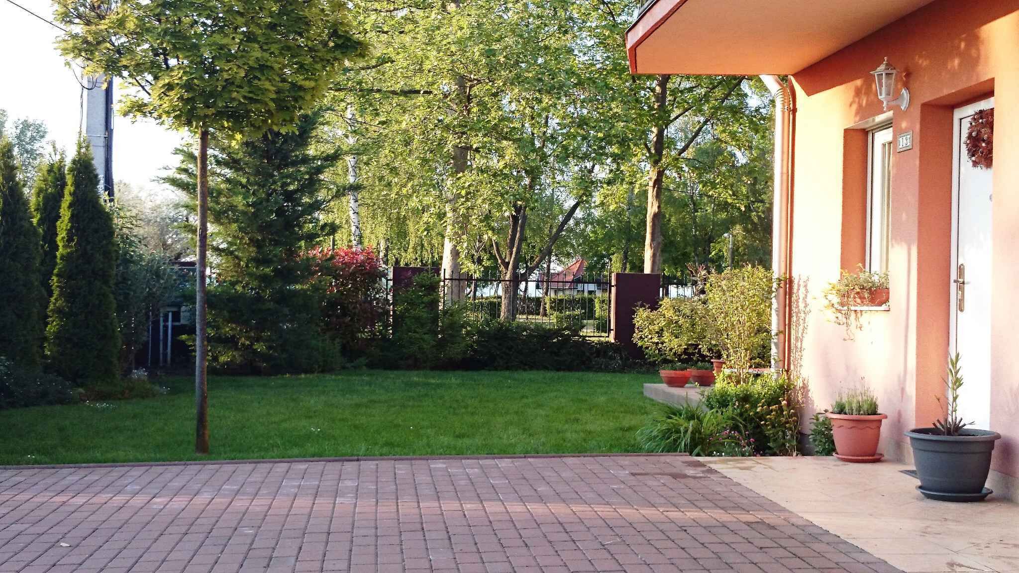 A paved patio area with a grassy lawn and trees in the background.
