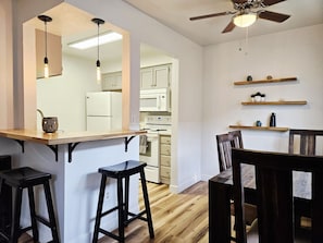 Una cocina con un refrigerador blanco, estufa y microondas. Hay taburetes de madera y una mesa de comedor de madera con sillas.