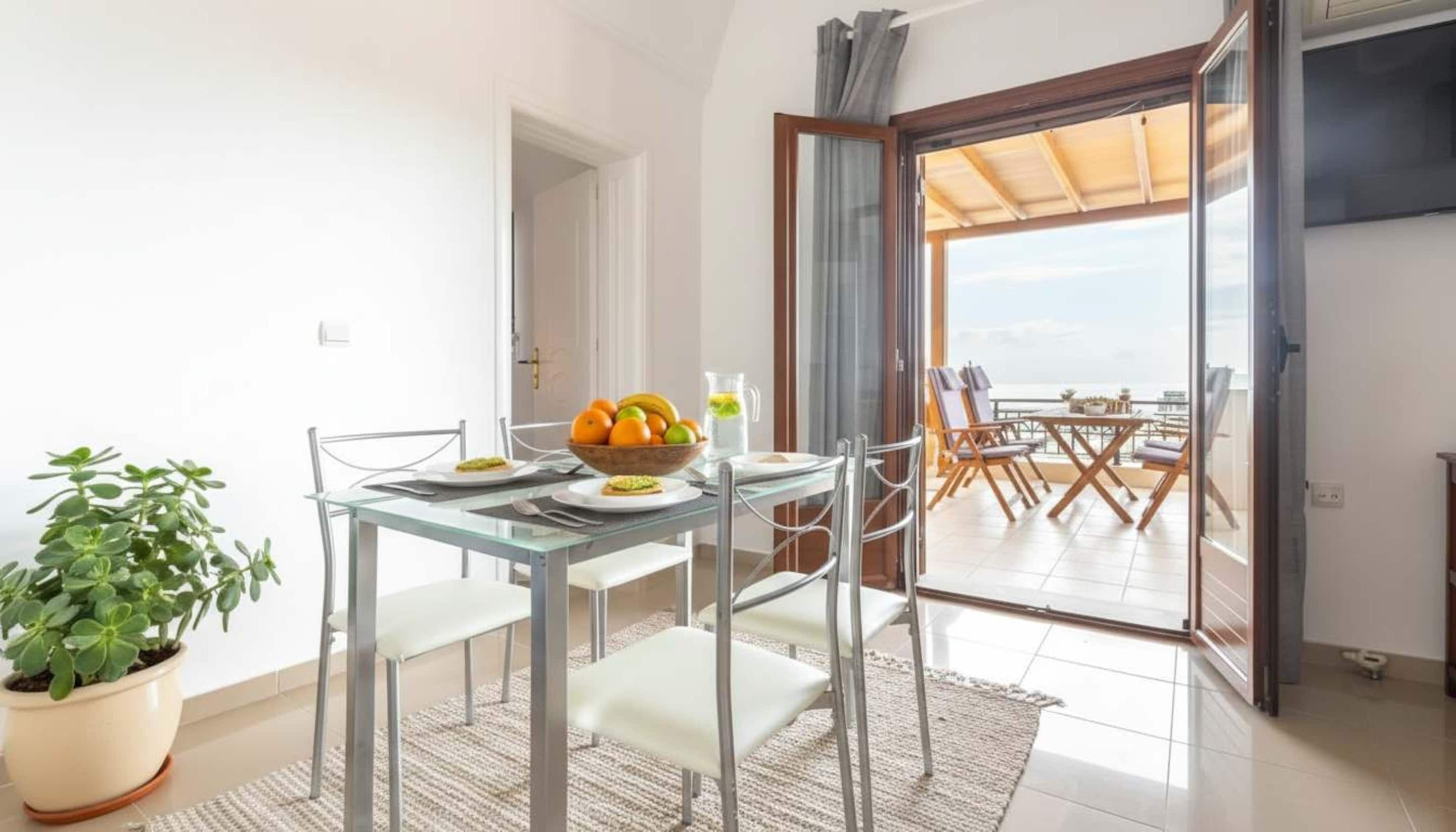 Un comedor con una mesa dispuesta para dos personas, un frutero y una planta en maceta.