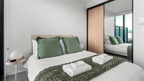 Ein modernes Hotelzimmer mit einem Bett, einem Nachttisch mit Lampe, einem großen Spiegel und Blick auf die Stadt.