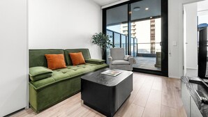 Ein modernes Wohnzimmer mit einem grünen Sofa, einem schwarzen Couchtisch und einem grauen Sessel.