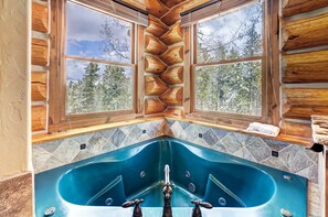 A log cabin interior with a large bathtub, stone-tiled walls, and a view of trees through large windows. - The Ski Classic Lodge - Hike in / out at Peak 8 in the best location in Breck (Breckenridge)