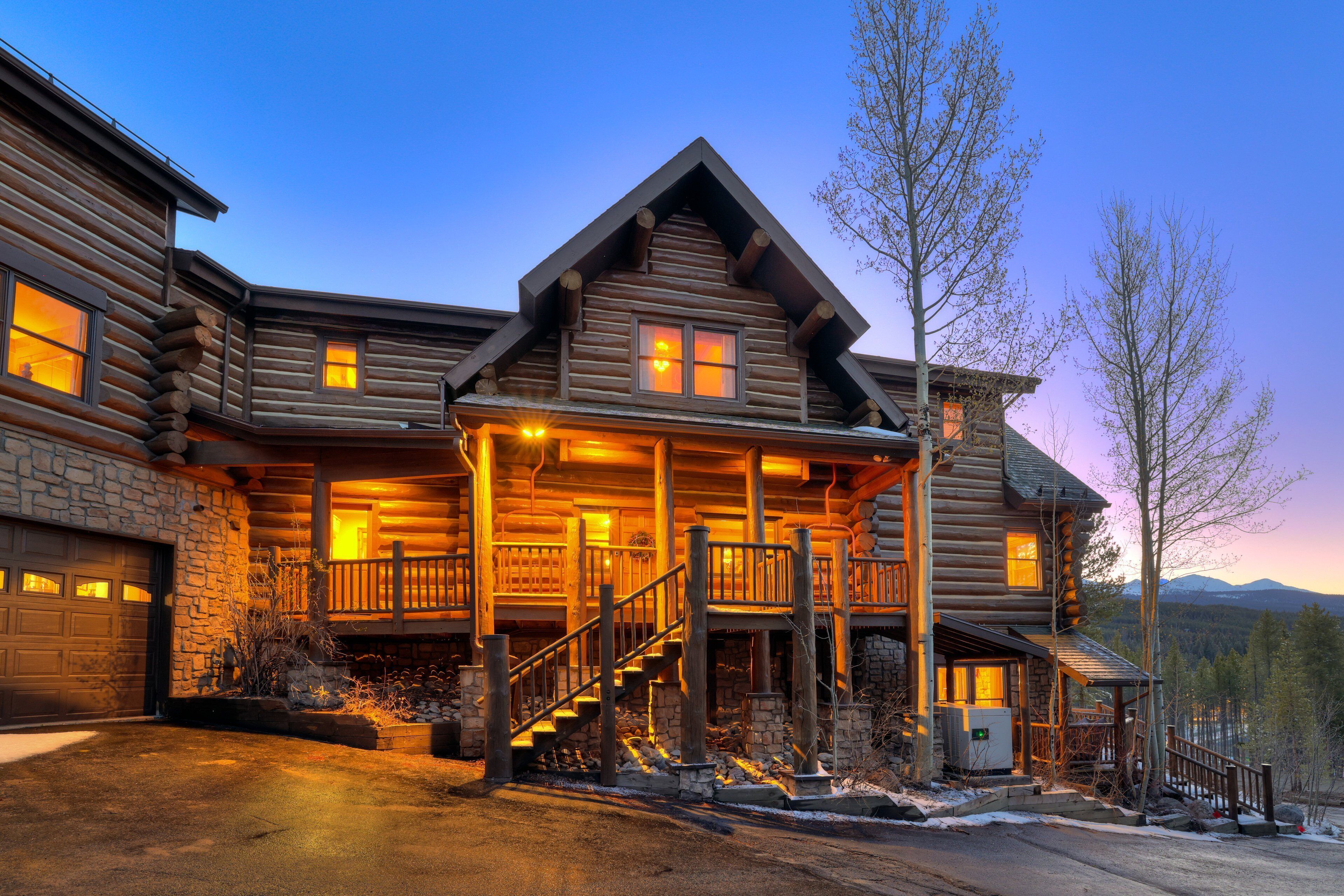 A log cabin with a stone foundation, multiple windows, a porch, and a staircase leading to the entrance.