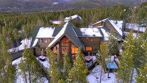 Une cabane en rondins avec une terrasse, entourée d’arbres couverts de neige et avec une montagne en arrière-plan.