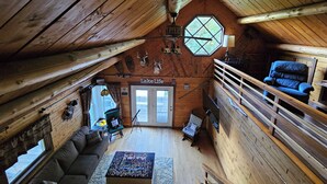 Interior acogedor de una cabaña con cama en altillo, un sofá, una mesa de centro y un cartel que dice 'Lake Life'.