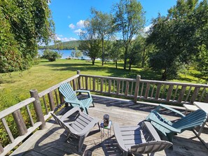 A wooden deck with lounge chairs and a table, overlooking a lake and greenery.