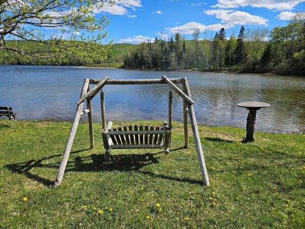 A wooden swing set by a lake with a bench and a table nearby. - Spaulding Lake Cottage: 4-acre lakefront retreat in Northern Maine (Oakfield)