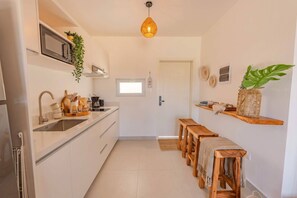 Eine kleine Küche mit Mikrowelle, Spüle, Holzschemeln und einer Pendelleuchte.