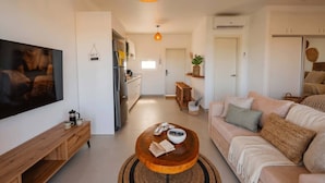 Ein modernes Wohnzimmer mit Fernseher, einem Holztisch, einer Couch und einer Küche im Hintergrund.