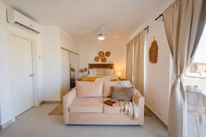 Ein Schlafzimmer mit einem Bett, einer Schlafcouch, einem Deckenventilator und einem Fenster mit Vorhängen.