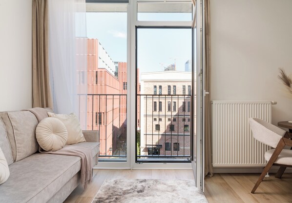 A modern living room with a sofa, a dining table, and a view of buildings through a large window. - Browary Warszawskie Harmony Studio (Warszawa)